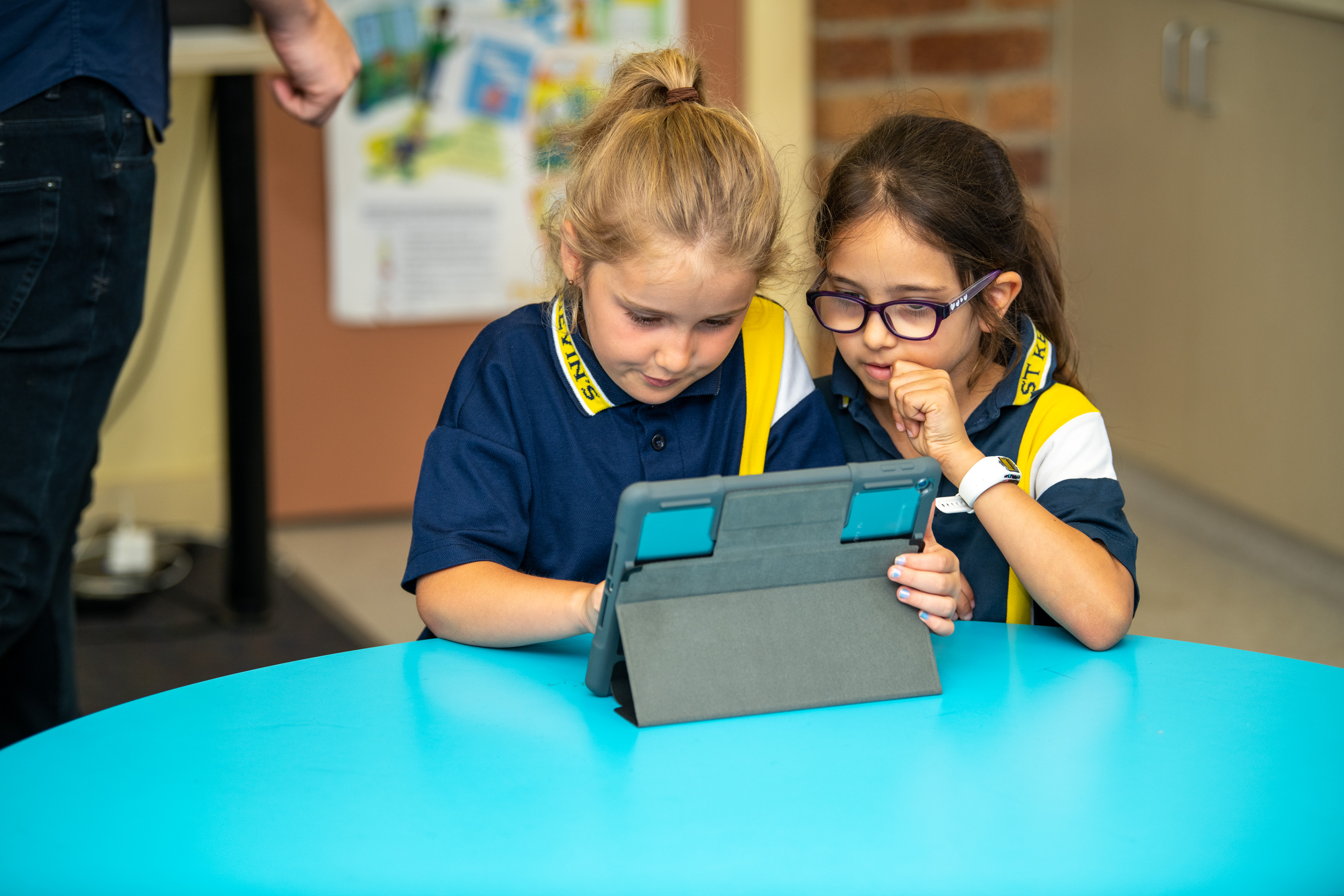 Two primary aged students sitting at a desk with an iPad.